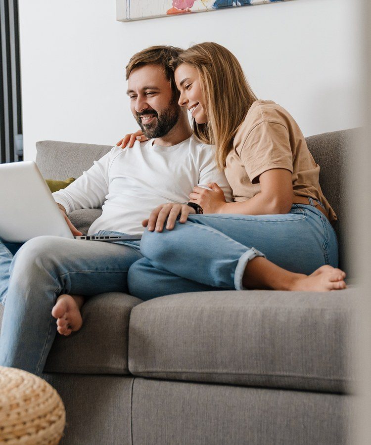 A smiling couple looking at a laptop on their couch